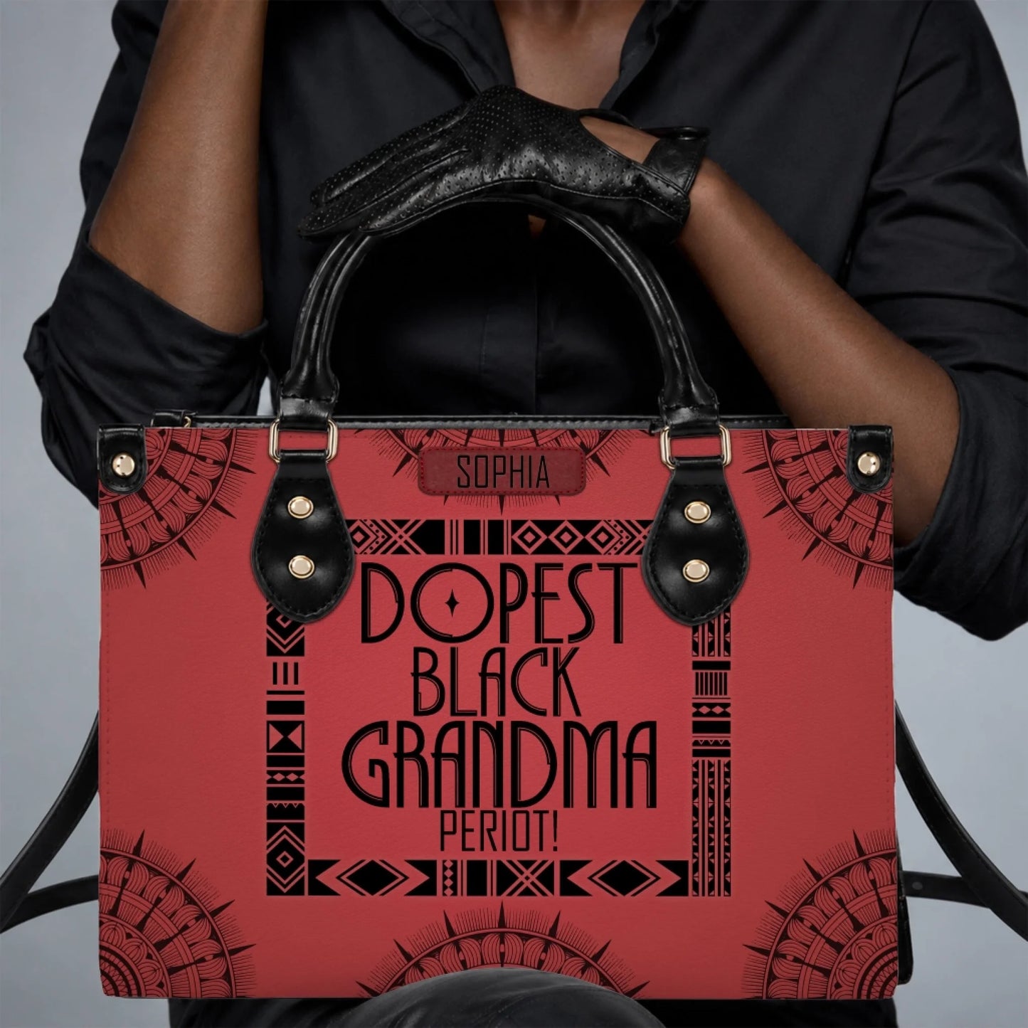 Close up of a person wearing black gloves holding a personalized red handbag labeled Dopest Black Grandma Period.