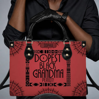 Close up of a person wearing black gloves holding a personalized red handbag labeled Dopest Black Grandma Period.