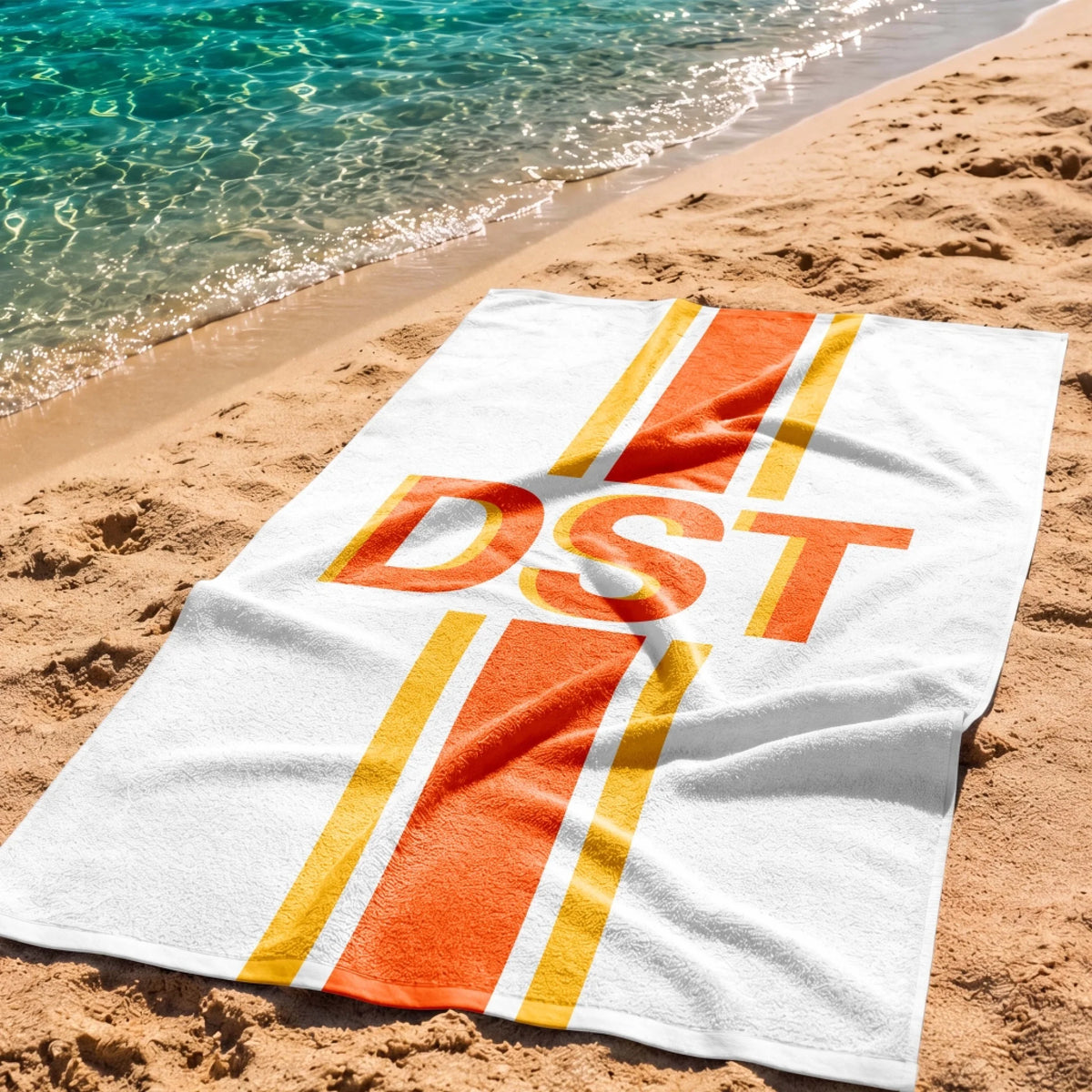 Customized DST print beach towel displayed on a tropical sandy shore near clear blue ocean water for summer fun.