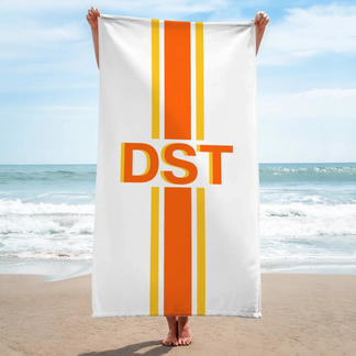 A person holding up a white personalized beach towel with an orange DST monogram and vertical orange and yellow stripes.