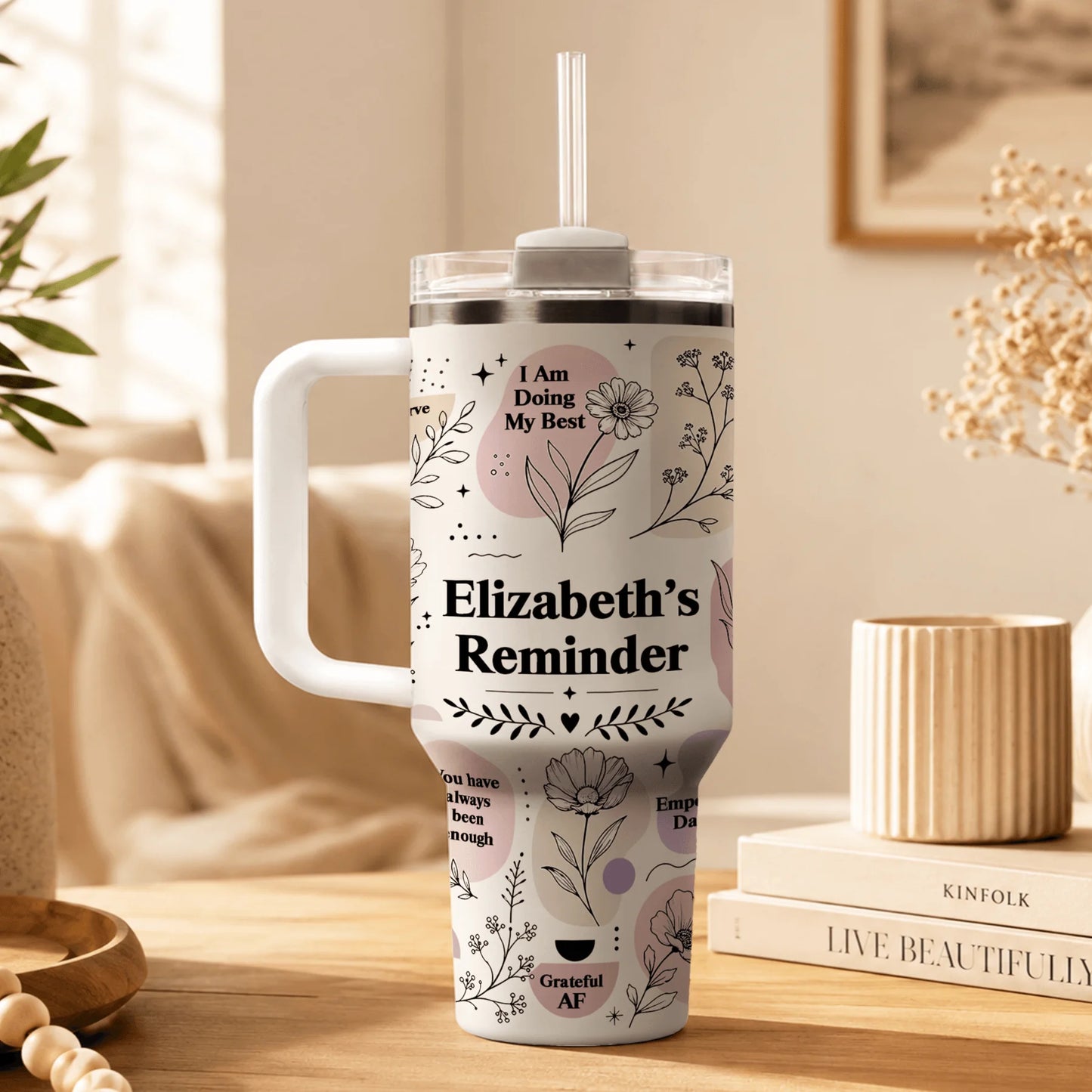Custom tumbler featuring floral illustrations, abstract shapes, and the text Elizabeth's Reminder on a desk.