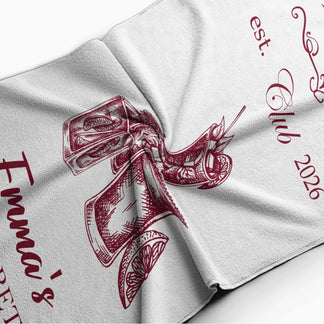 Close up view of a personalized bachelorette beach towel featuring cocktail art and custom party text details.