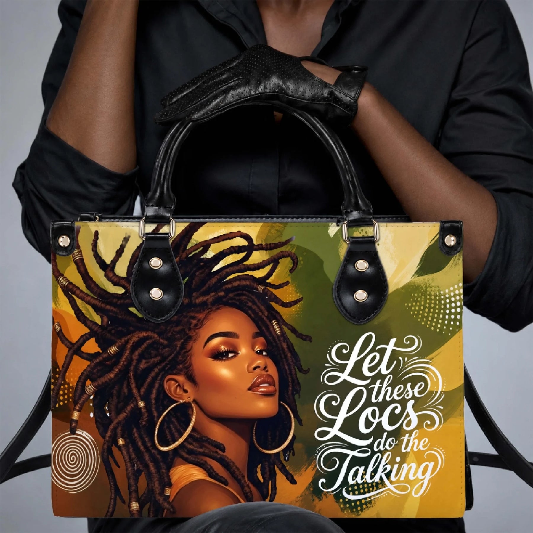 A person holding a stylish black handbag with an artistic graphic of a woman with locs and the text Let these Locs do the Talking.