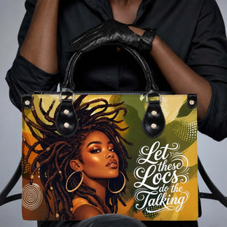A person holding a stylish black handbag with an artistic graphic of a woman with locs and the text Let these Locs do the Talking.