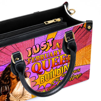 Close up of a personalized february queen empire handbag featuring high quality black handles and gold hardware.