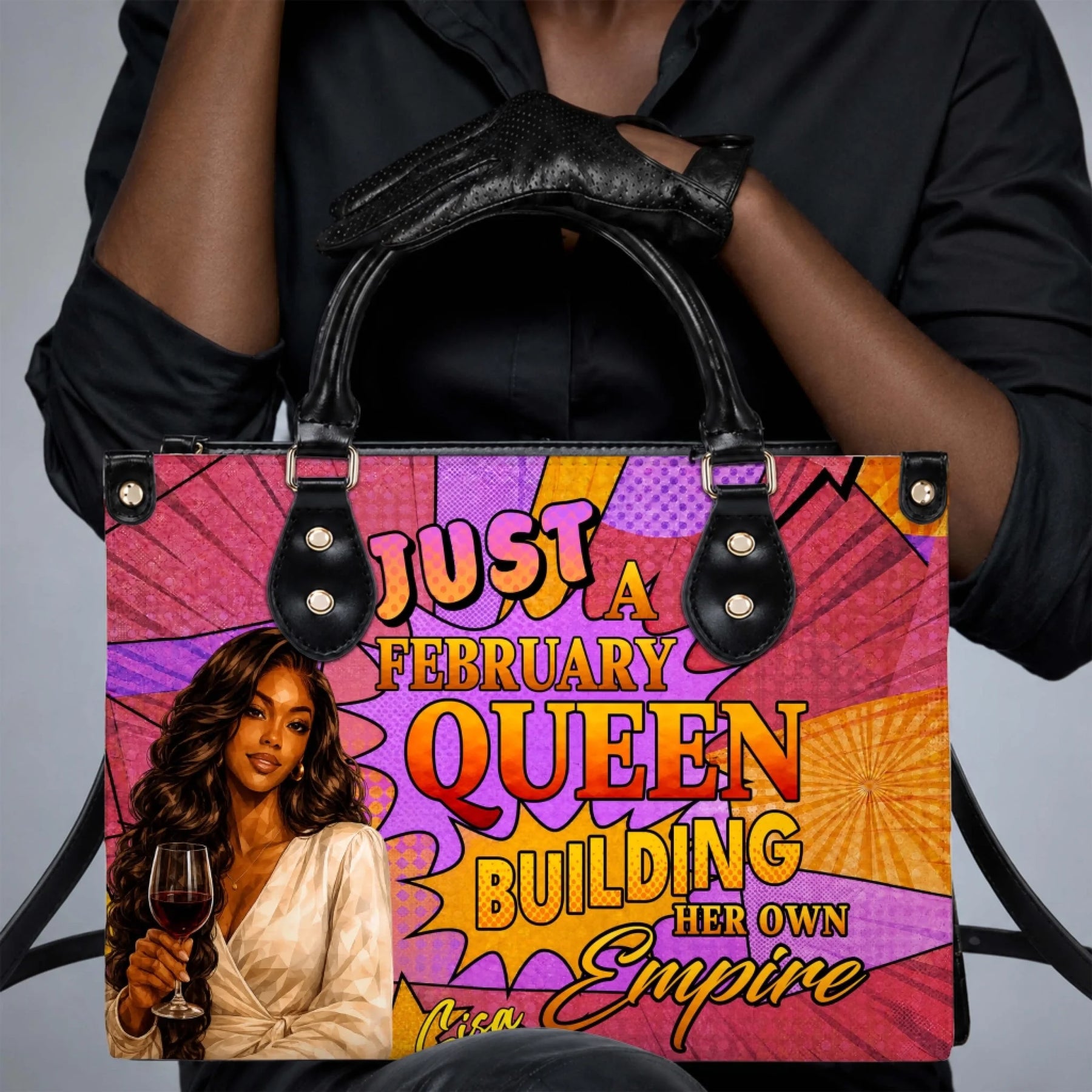 Black gloved hands holding a vibrant february queen handbag with empowering graphic text and a wine glass illustration.