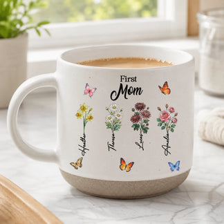 A white ceramic mug labeled 'First Mom' featuring individual floral bouquets with names and colorful butterflies.