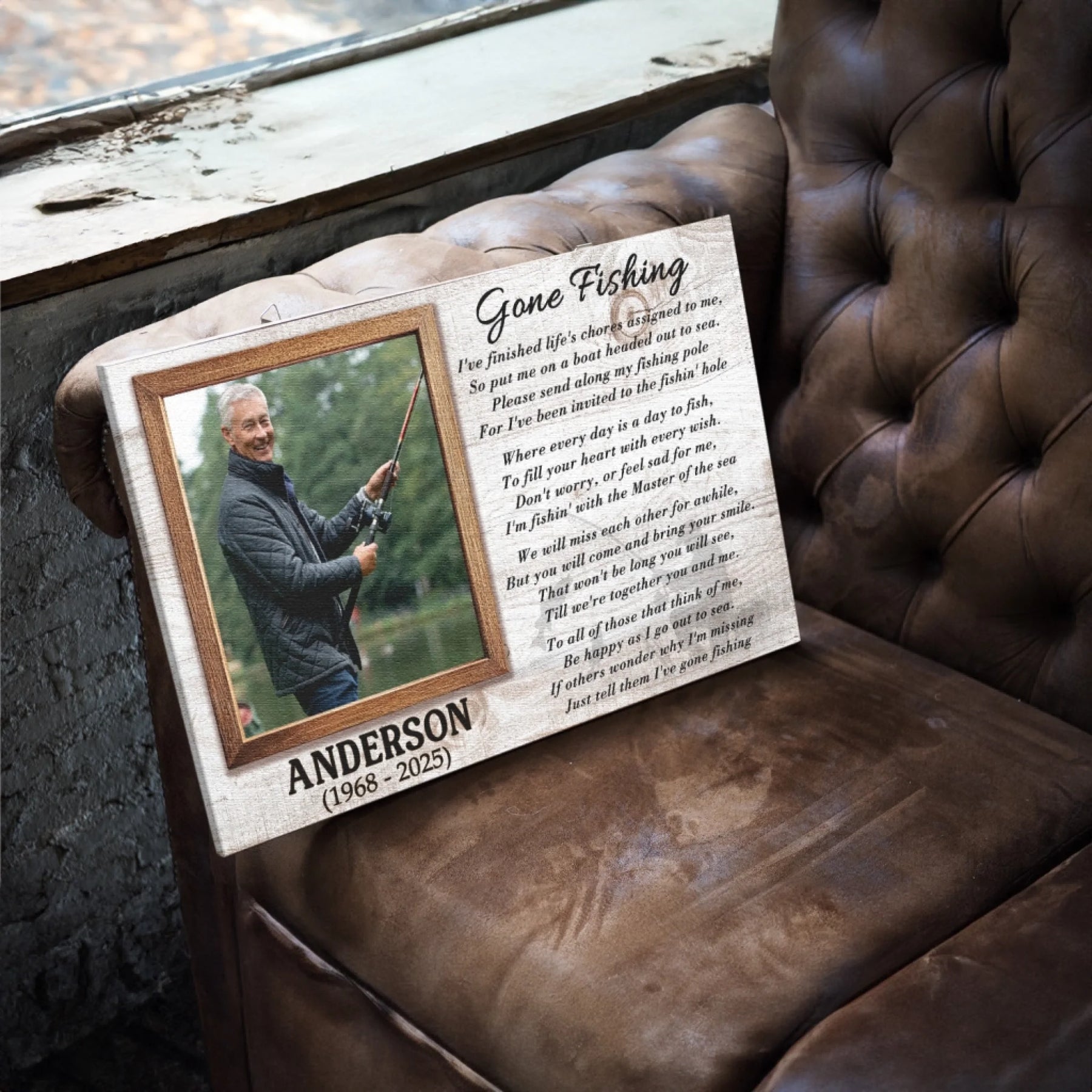 A rectangular canvas print featuring a photo of a man fishing, a poem, and a name, resting on a brown leather armchair.