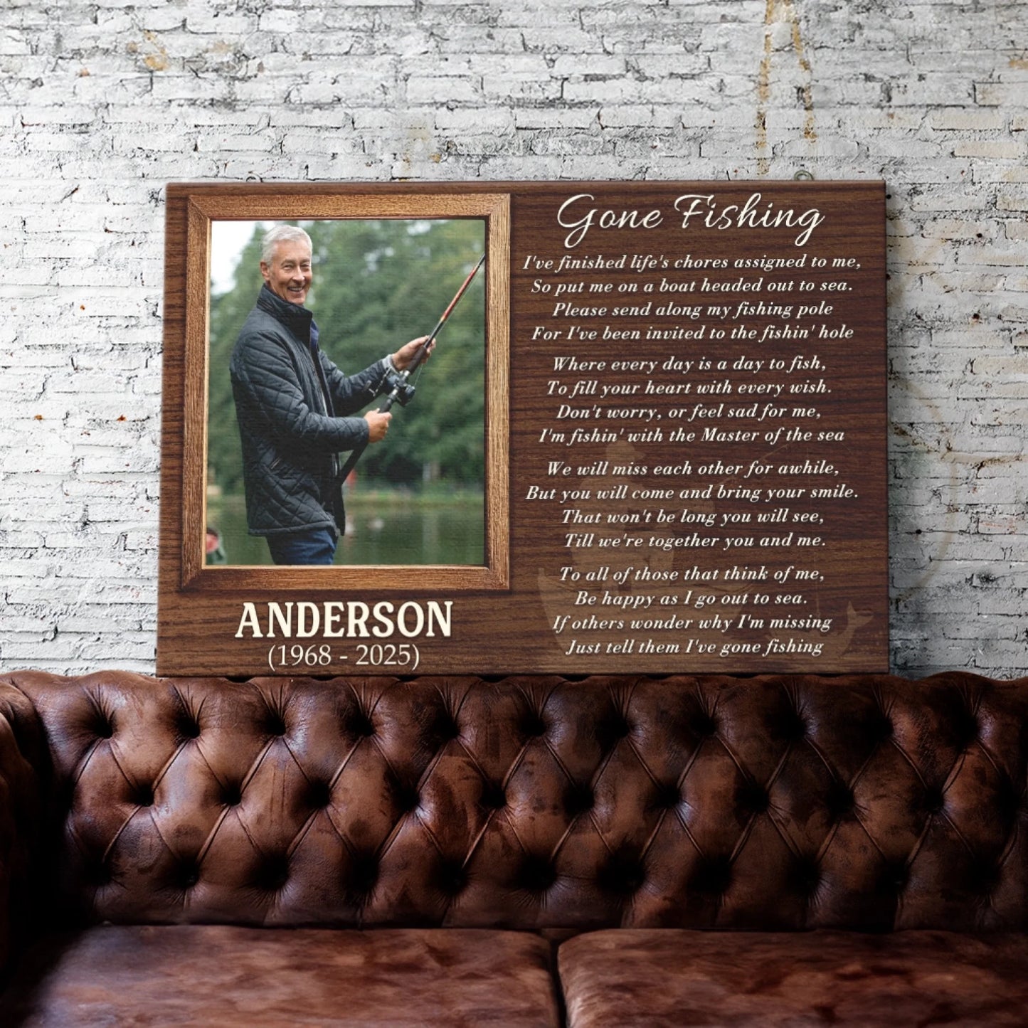 A wooden plaque with a fishing photo and poem is displayed on a distressed brick wall above a brown tufted leather sofa.