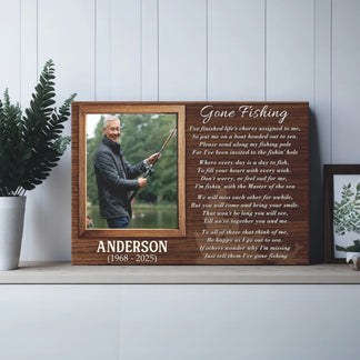 A wooden plaque with a fishing photo and poem rests on a shelf in a room with a green plant and a framed botanical print on the right.