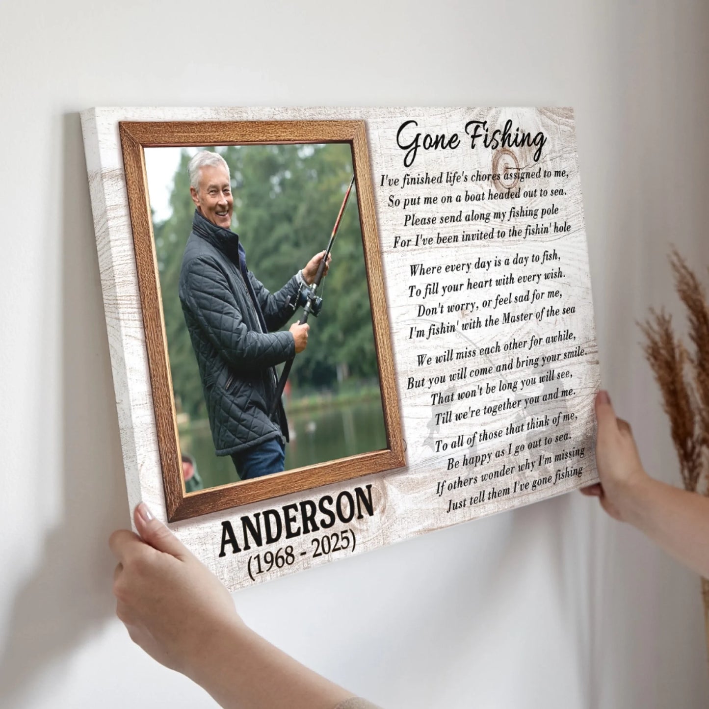 A rectangular canvas print featuring a photo of a smiling man fishing, a poem, and a name, held by two hands.