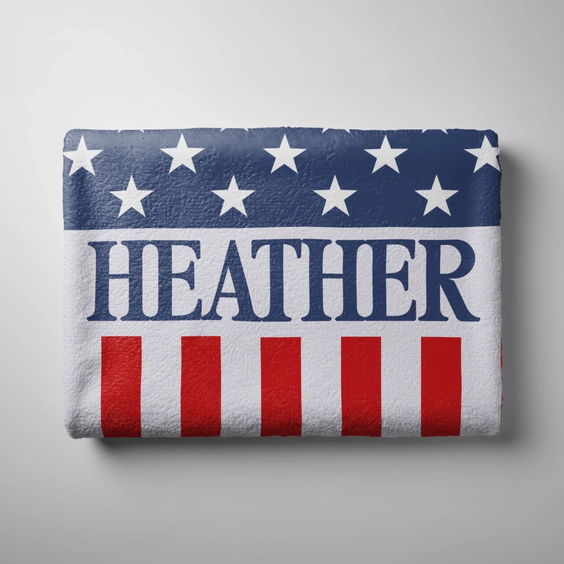 A folded personalized beach towel with an American flag theme and the custom name Heather centered in blue.