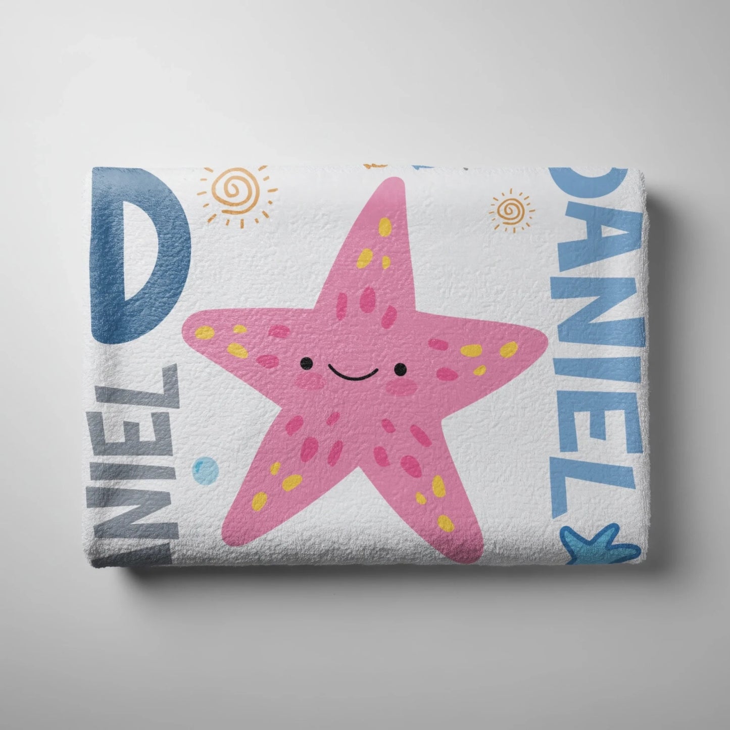 Folded personalized beach towel for children featuring a cute pink starfish design and the name Daniel.