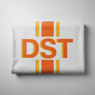 A neatly folded white beach towel with a vibrant orange DST monogram and vertical stripe design on a plain background.