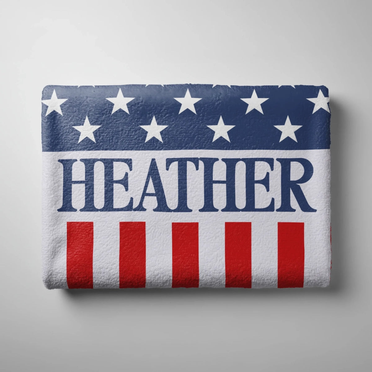 A neatly folded patriotic beach towel featuring a stars and stripes design with the custom name Heather in the center.