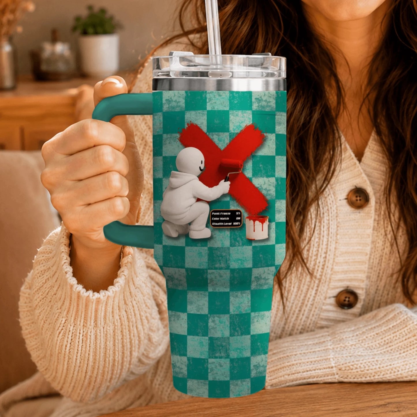 Hand holding a personalized gaming tumbler featuring a white character painting a red X on teal checkered