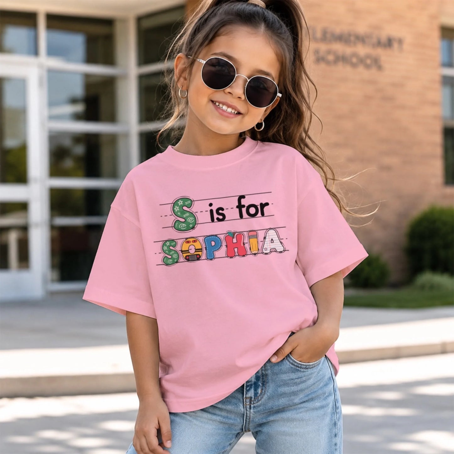 A girl with sunglasses wearing a pink personalized back to school t-shirt featuring the custom name Sophia.