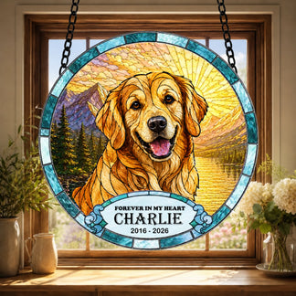 A round stained-glass style suncatcher hangs in a window, featuring a smiling golden dog against a mountain and lake scene. It includes a banner with memorial text.
