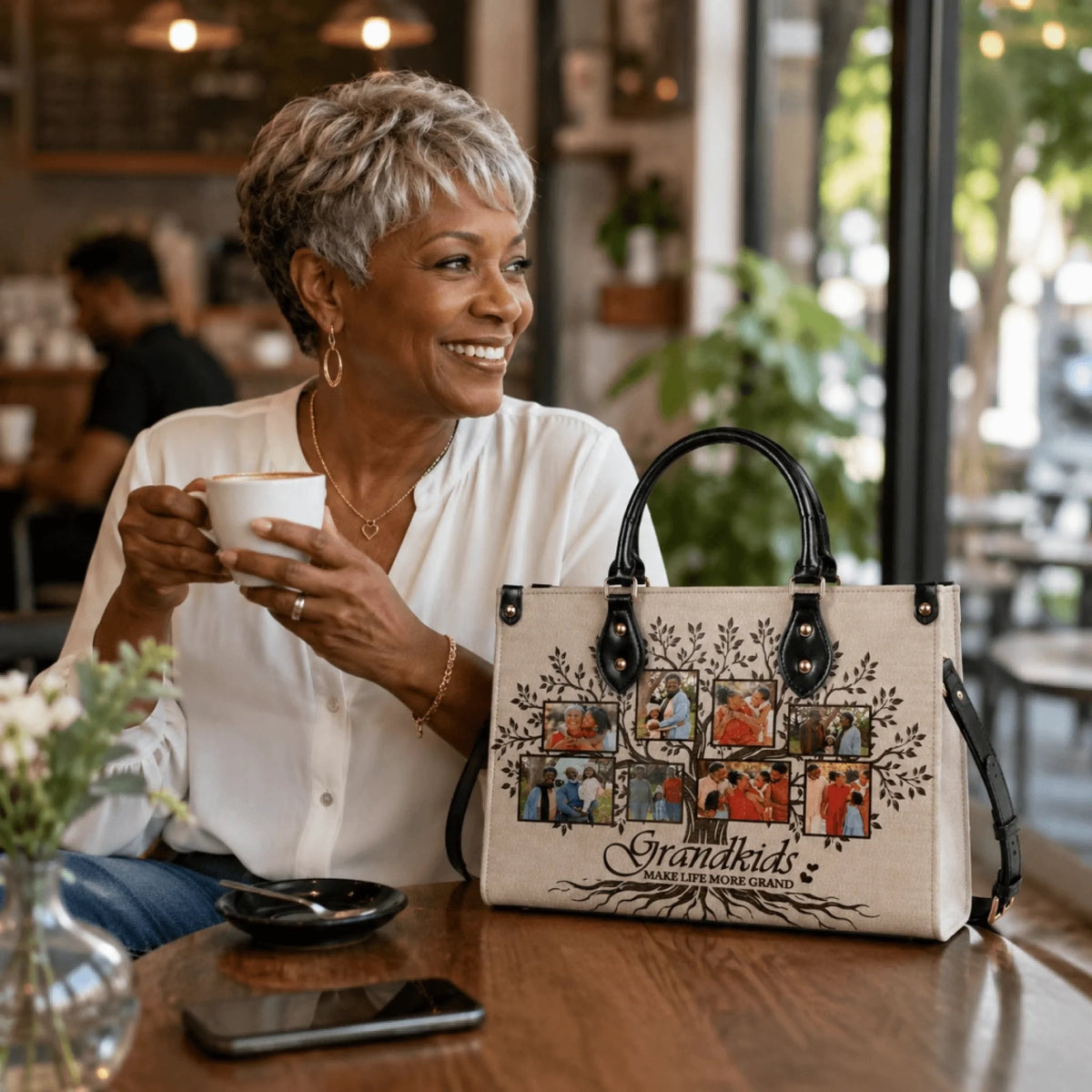 Smiling grandmother drinking coffee next to her personalized family tree handbag with photo prints of grandchildren.