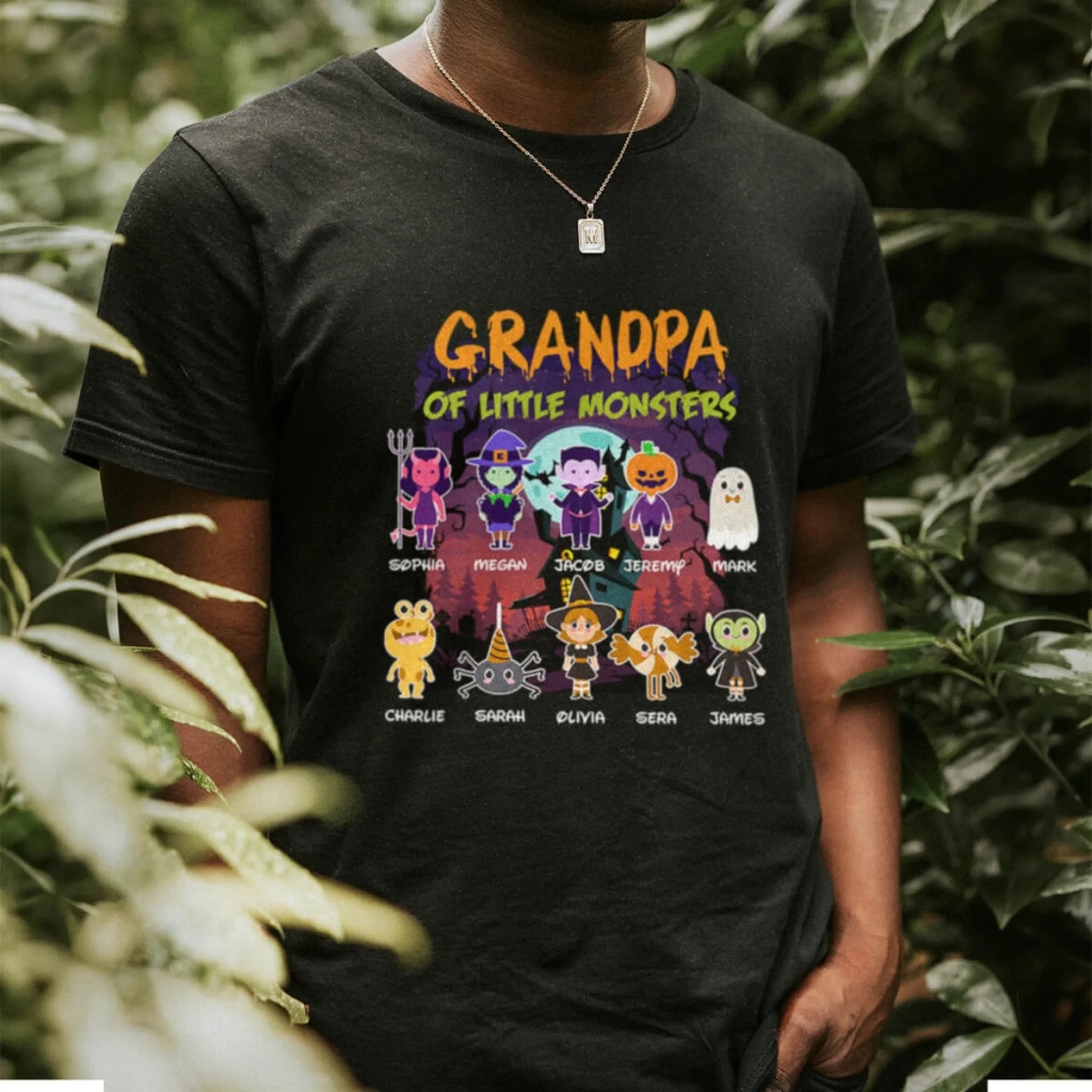 A man wears a black personalized Halloween t-shirt featuring a Grandpa of Little Monsters design with custom names.