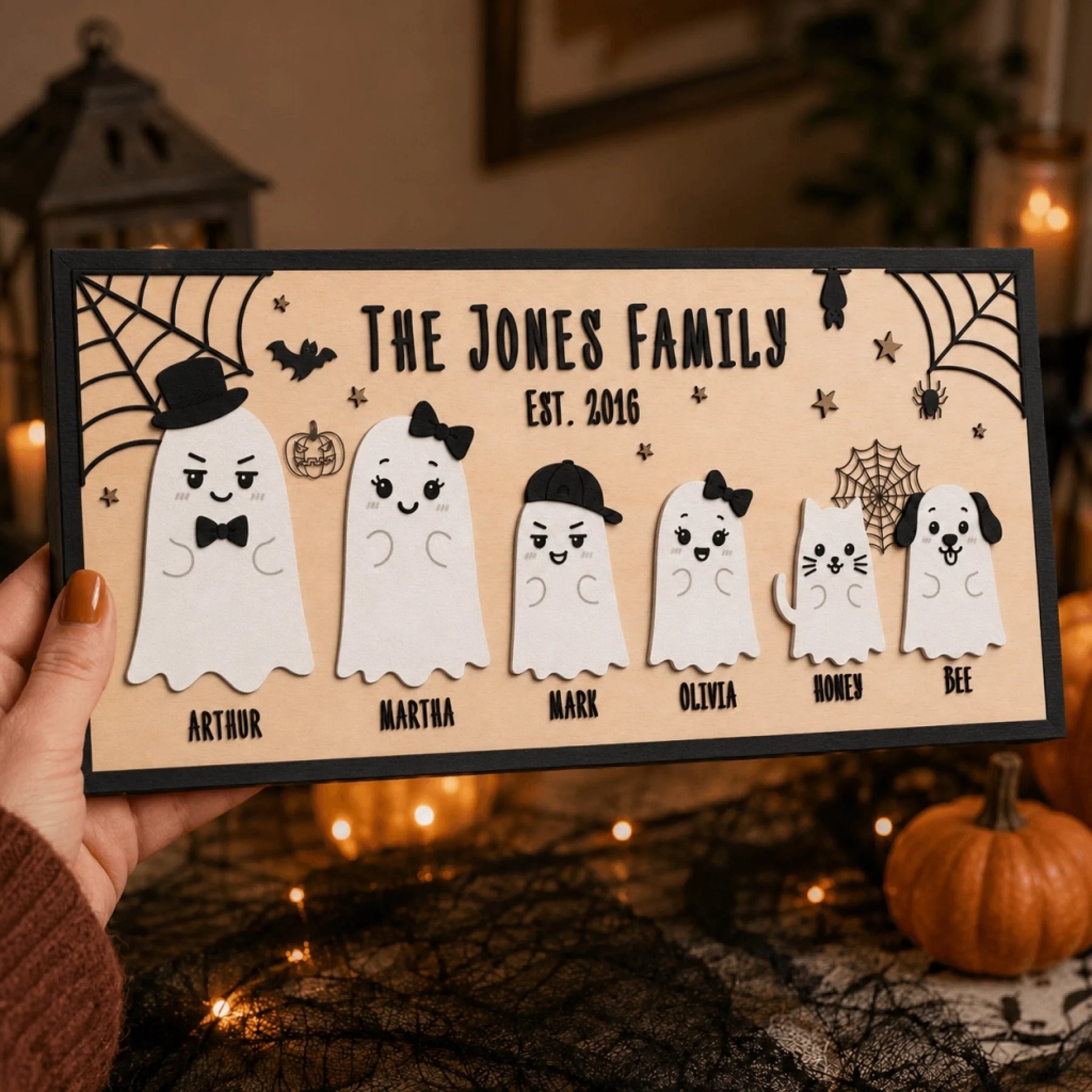 A hand holds a personalized wooden sign featuring a cute ghost family, perfect for Halloween family wall decor.