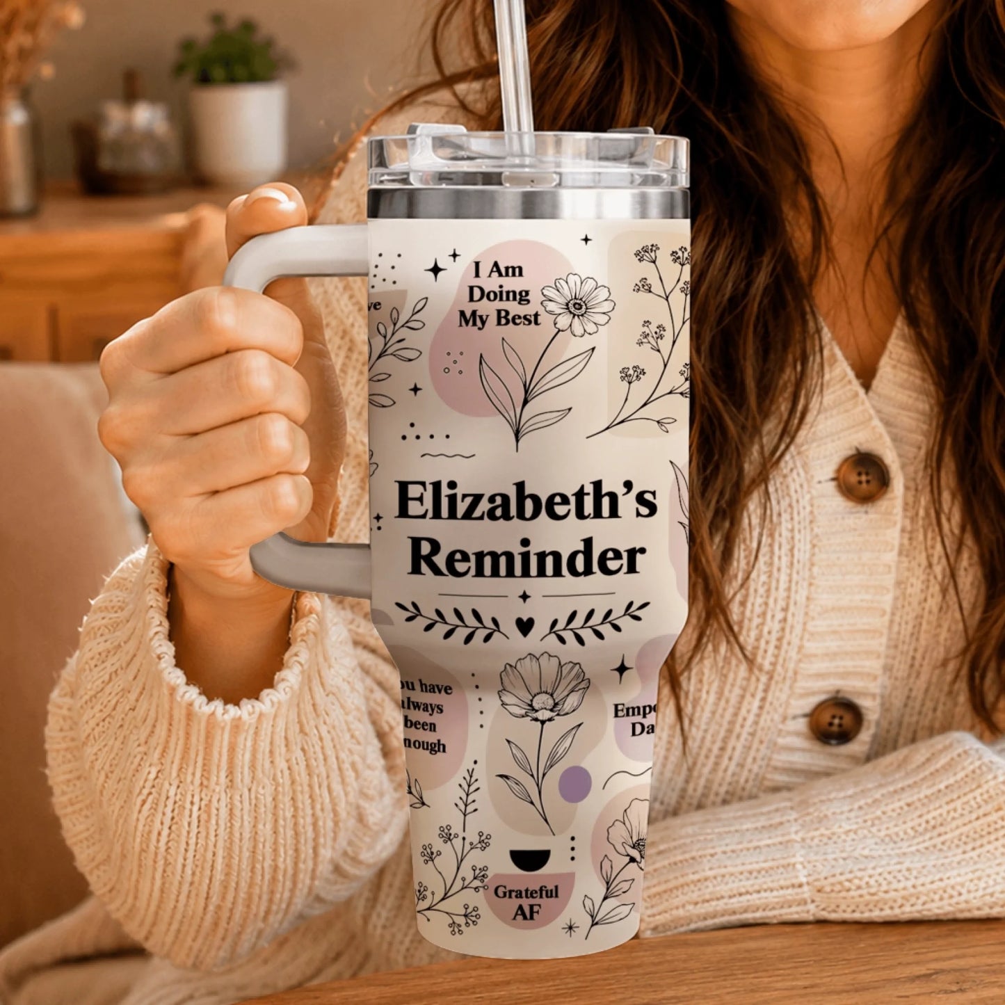 Close-up of a hand holding a personalized floral tumbler featuring the text Elizabeth's Reminder.