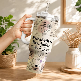 Close-up of a person holding a custom floral tumbler with the text Elizabeth's Reminder in a bright room.