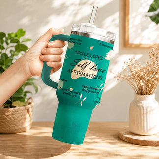 A hand holding a teal stainless steel tumbler decorated with inspiring self-love quotes and flower designs.