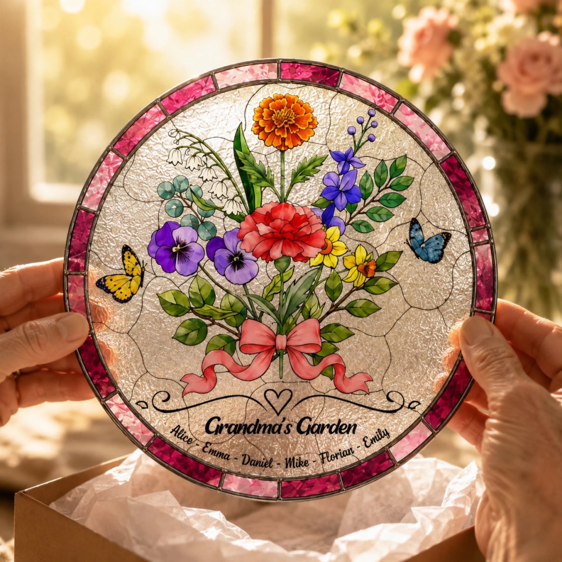 Hands holding Grandma personalized glass suncatcher with flowers, butterflies, and grandkids names in warm sunlight