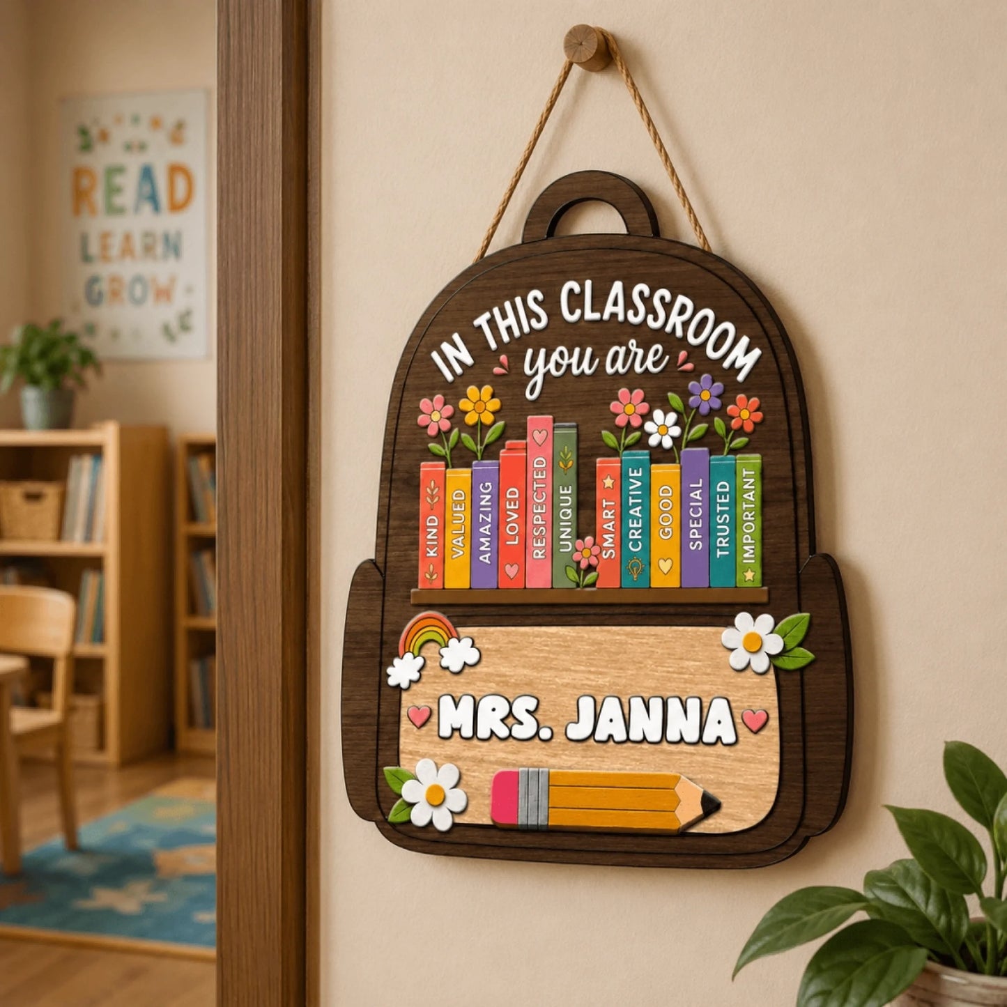 A backpack-shaped wooden sign hanging on a wall, featuring educational affirmations, flowers, and 'Mrs. Janna' text.