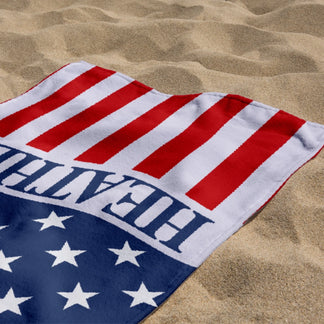 A personalized American flag beach towel featuring the name Heather lying on the sand at the beach for summer holidays.