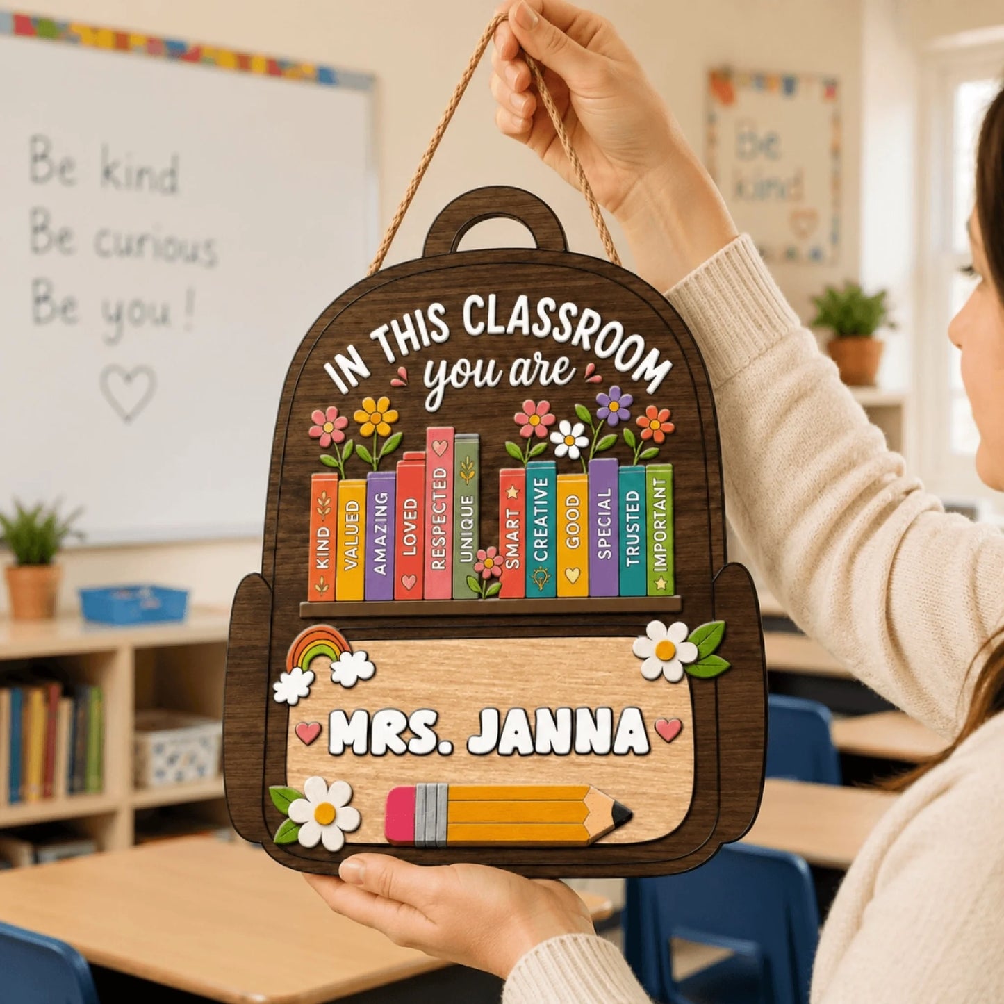 Hands holding a custom wooden backpack sign for teachers with classroom affirmations and 'Mrs. Janna' written on it.