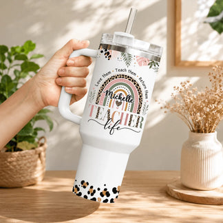 A hand holding a custom teacher life stainless steel tumbler with a leopard print rainbow pattern and personalized name.