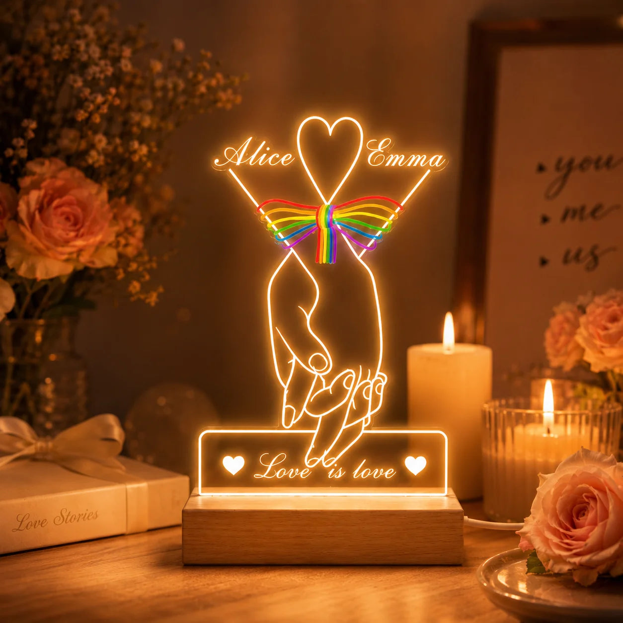 Decorative LED lamp with 'Love is love' message on a table with candles and flowers.