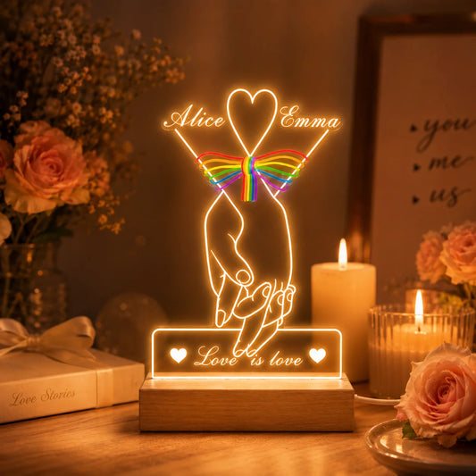 Decorative LED lamp with 'Love is love' message on a table with candles and flowers.