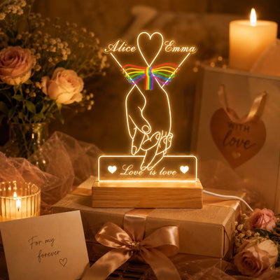 Decorative LED lamp with 'Alice & Emma' and rainbow heart design, surrounded by flowers and candles.
