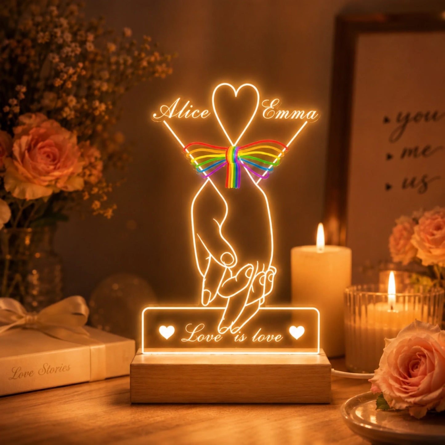 Decorative LED lamp with 'Love is love' message on a table with candles and flowers.