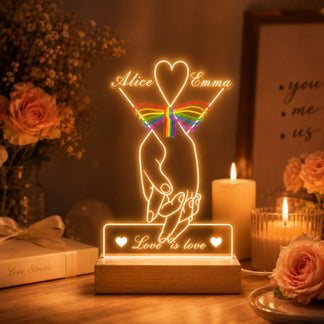 Decorative LED lamp with 'Love is love' message on a table with candles and flowers.