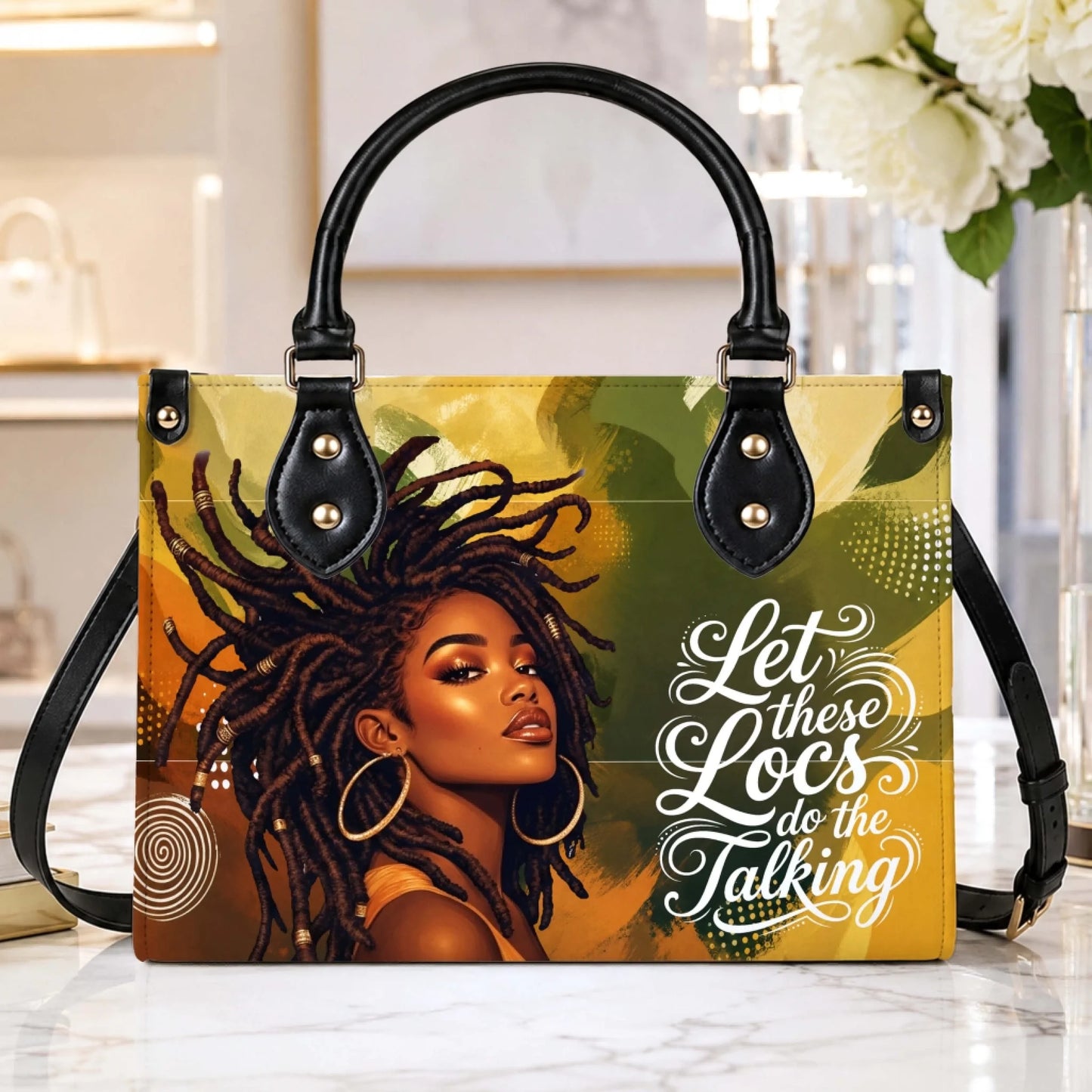 A beautifully designed handbag displayed on a table featuring bold artwork of a woman with locs and encouraging lettering.