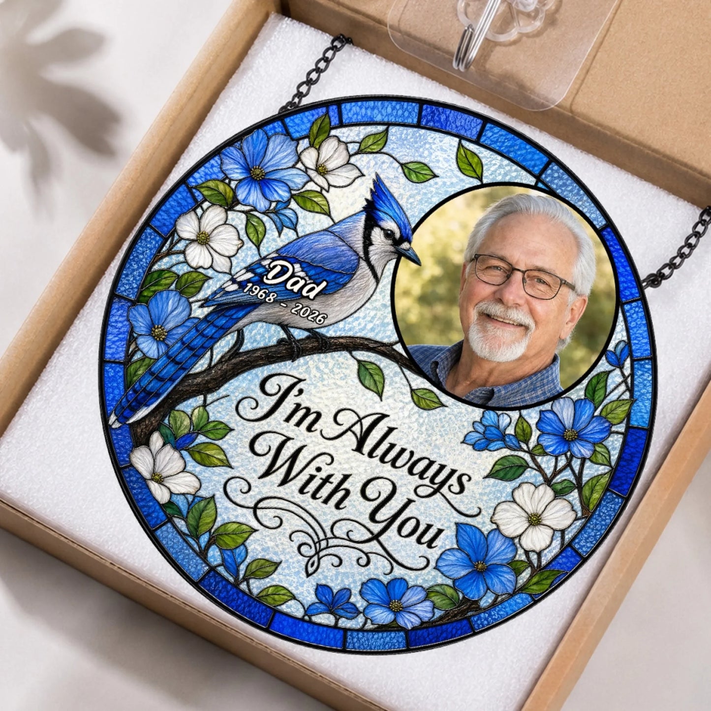 A round stained glass memorial suncatcher with a blue jay and photo in its original protective retail packaging.