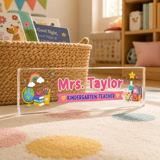 A clear personalized acrylic plaque desk sign for a kindergarten teacher featuring a colorful school supplies design.