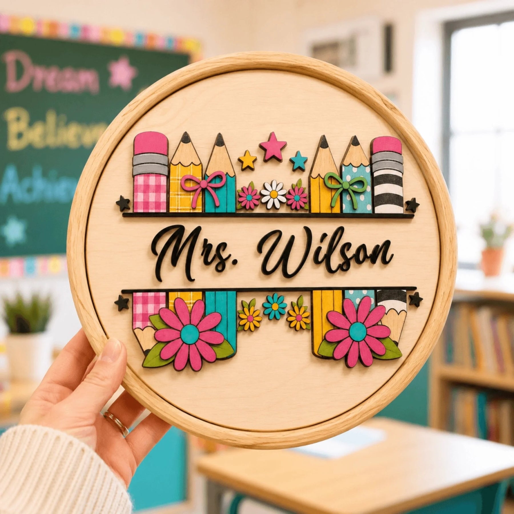 Hand holding a round custom classroom sign for Mrs Wilson with pencil and floral decorations.