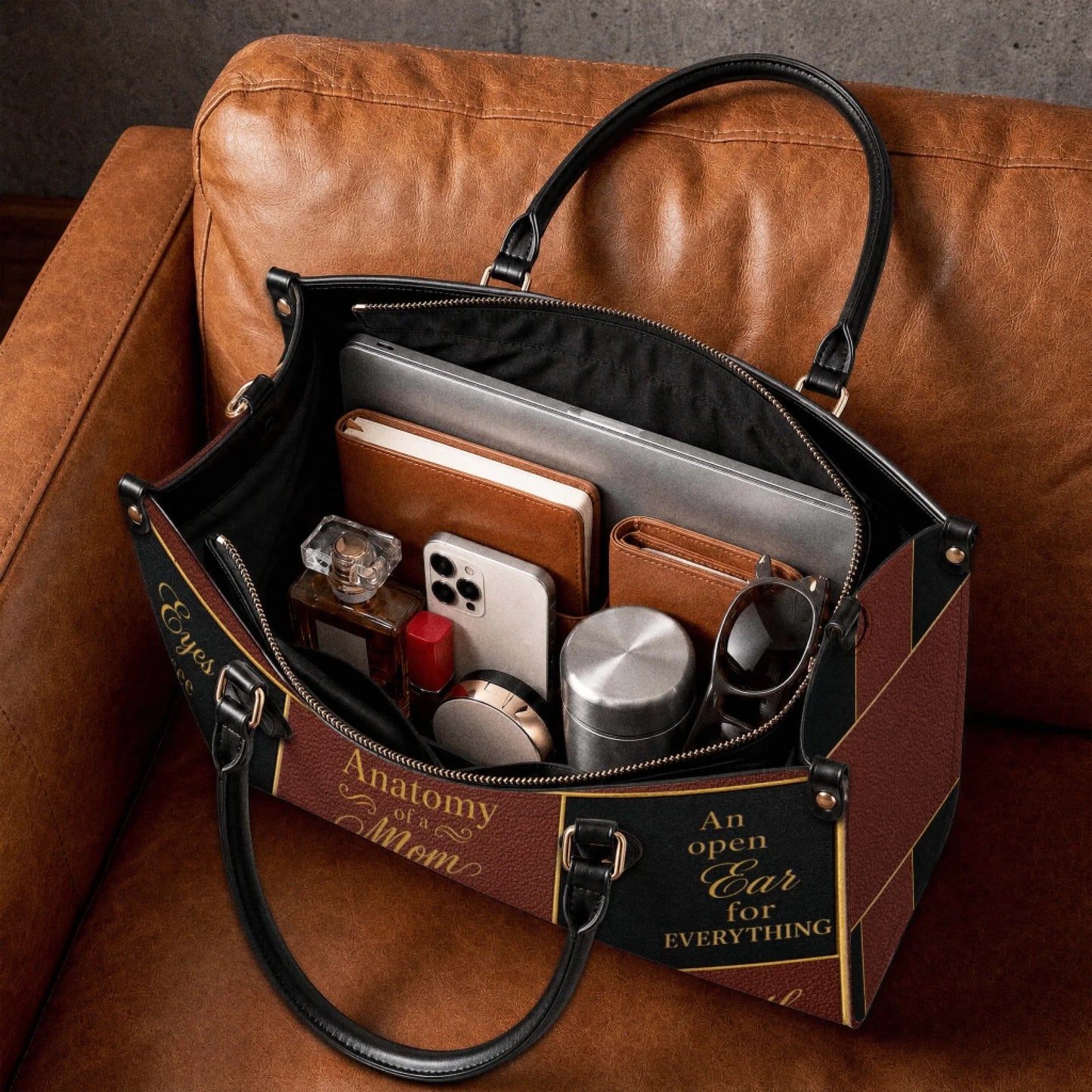 Open Anatomy of a Mom shoulder bag filled with everyday essentials like a laptop notebook phone and cosmetic items.