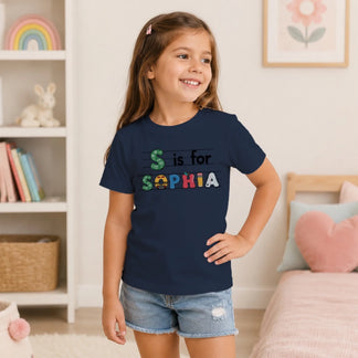 A young girl wearing a navy blue back to school t-shirt featuring her custom name Sophia in artistic colorful letters.