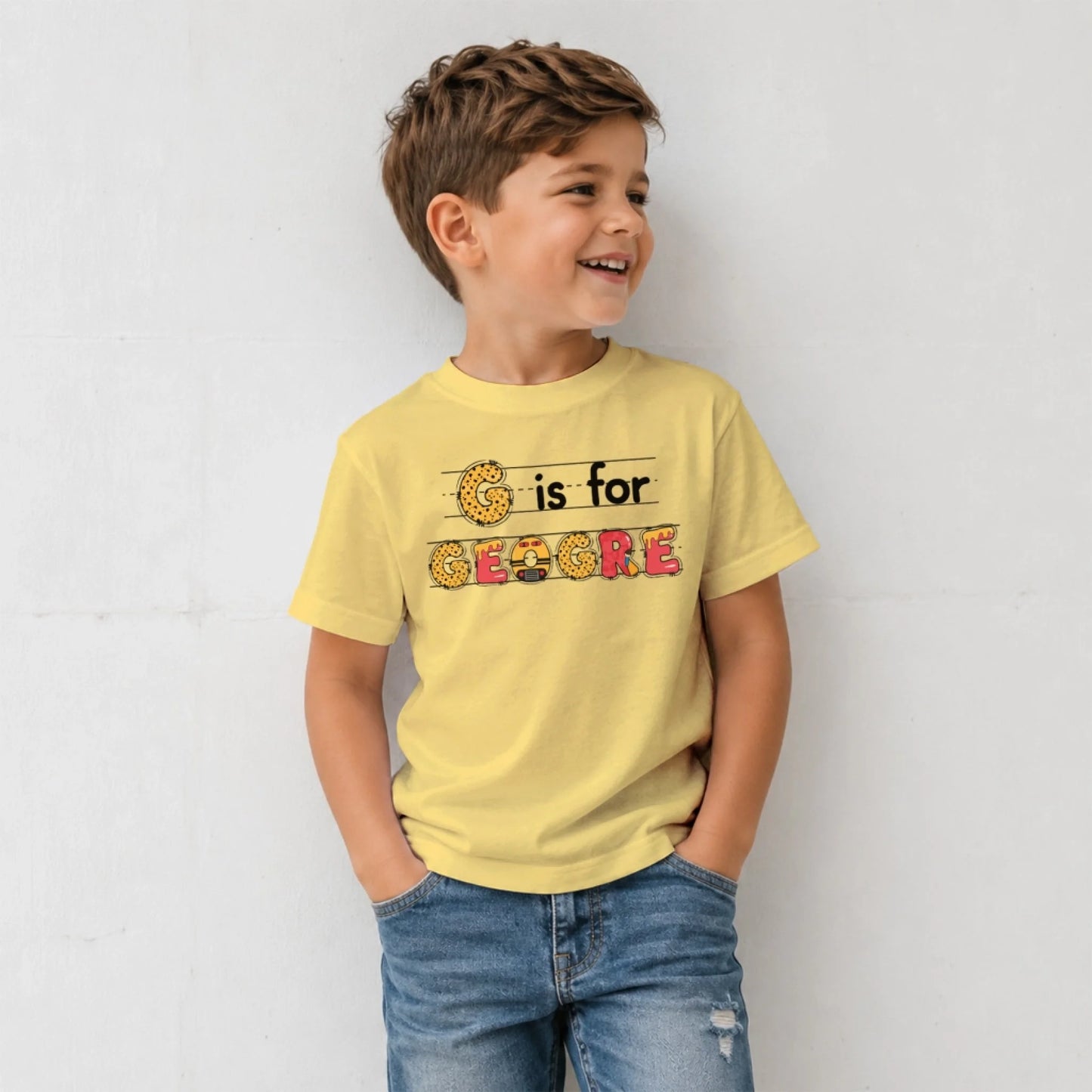 A young boy wearing a yellow back to school t-shirt personalized with the custom name Geogre in colorful letter art.