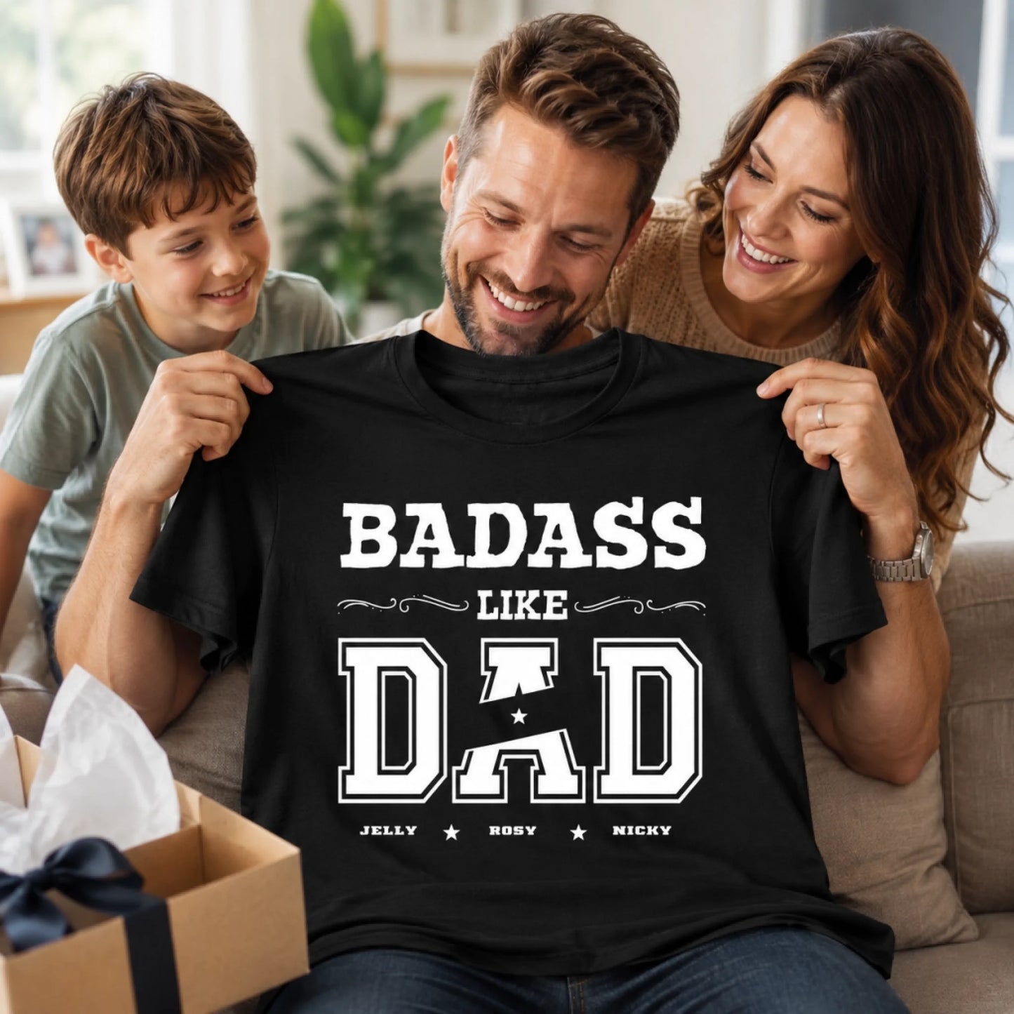 Man wearing a black t-shirt with 'BADASS LIKE DAD' text, surrounded by a woman and a child in a home setting.