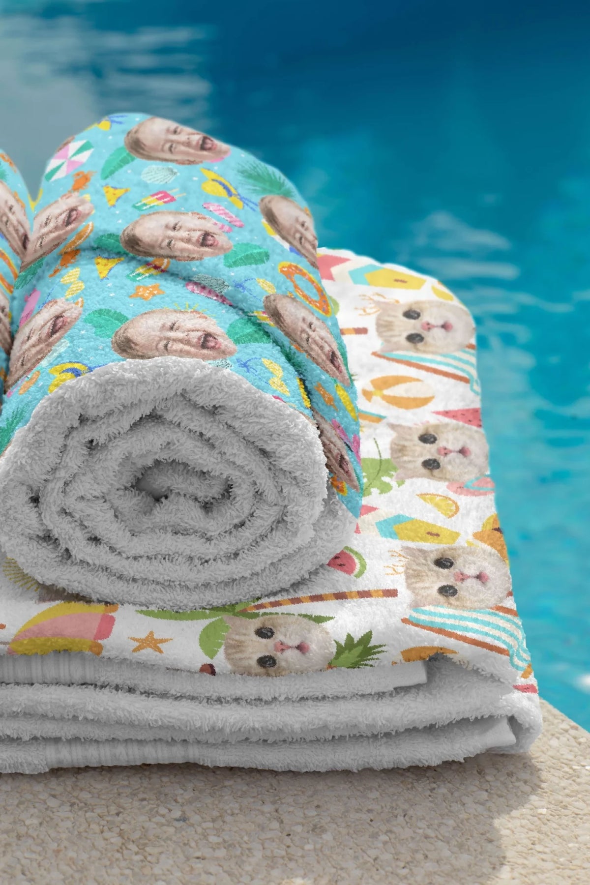 Rolled and folded personalized beach towels with custom photo prints of faces and pets next to a swimming pool.