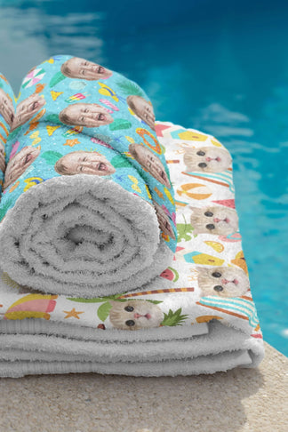 Rolled and folded personalized beach towels with custom photo prints of faces and pets next to a swimming pool.