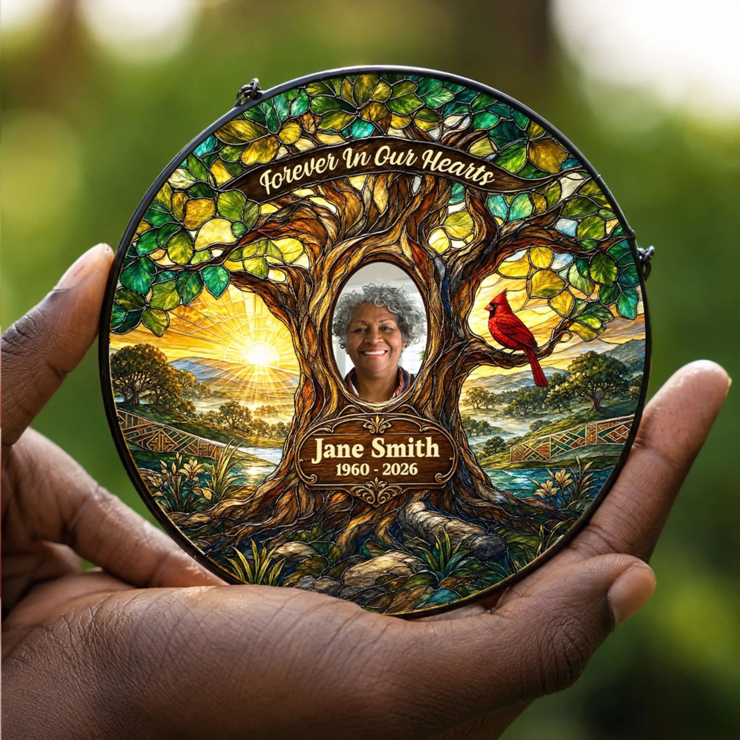 A personalized bereavement suncatcher held in hand, featuring a stained glass style tree, red cardinal, photo, and custom text.