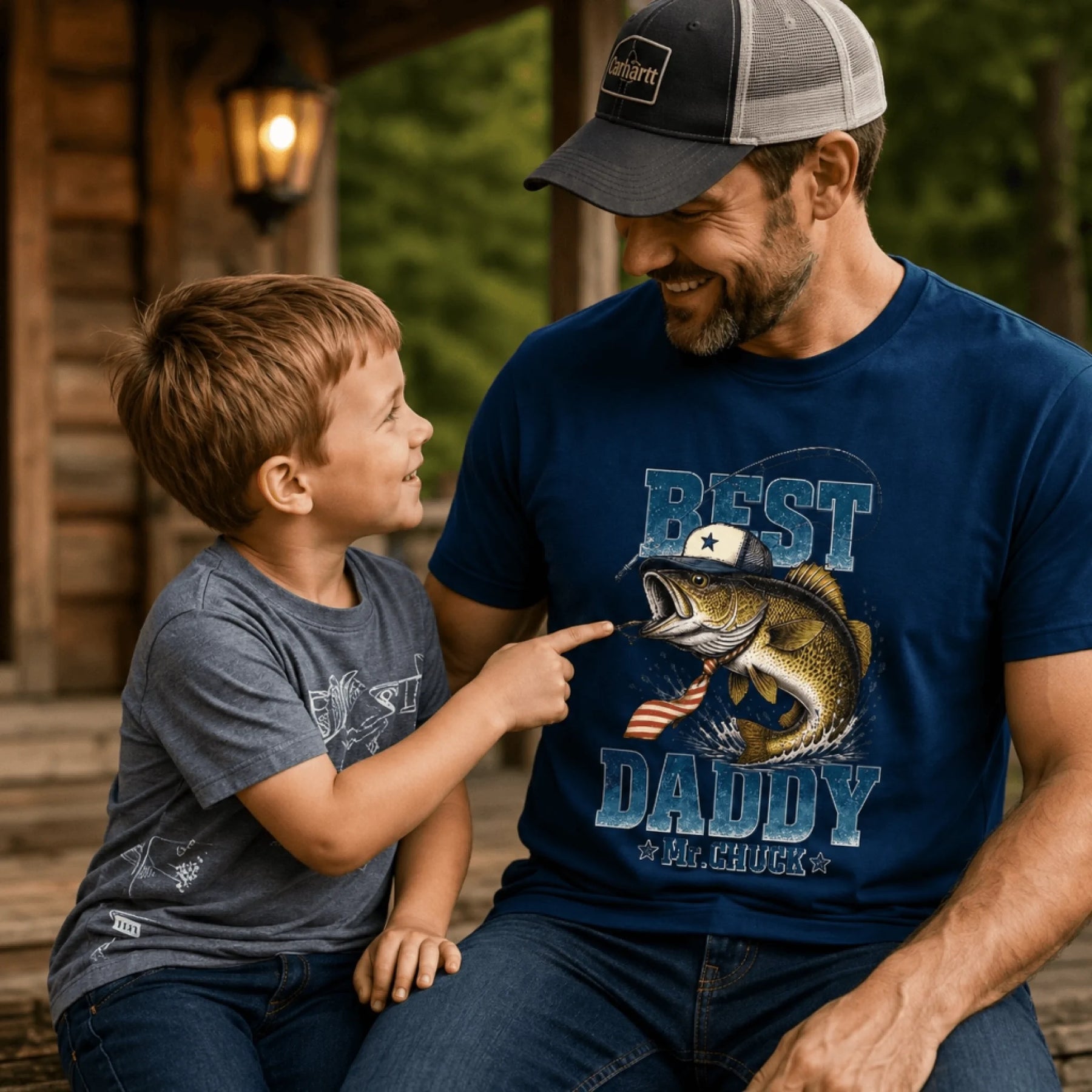 Man and child sitting together, both wearing matching t-shirts with a fish graphic and text.